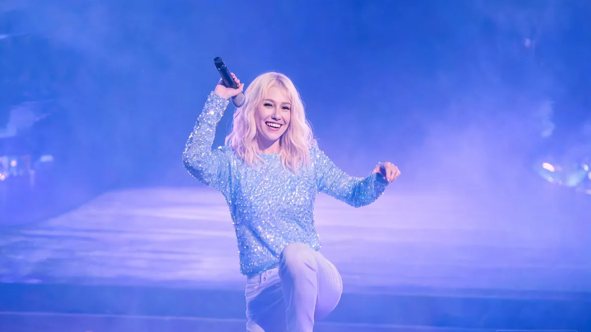 The defining idol traits in action, a cute pastel stage outfit with frills, twin tails, and a bright stage smile, the look fans cheer for at concerts