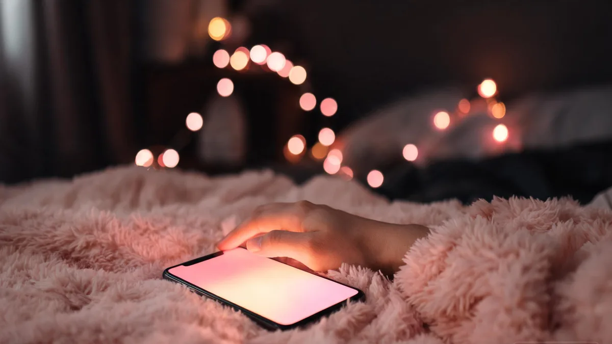 NSFW AI girlfriend companion accessed through a softly glowing phone in a cozy bedroom, an opt-in private space for adult chat