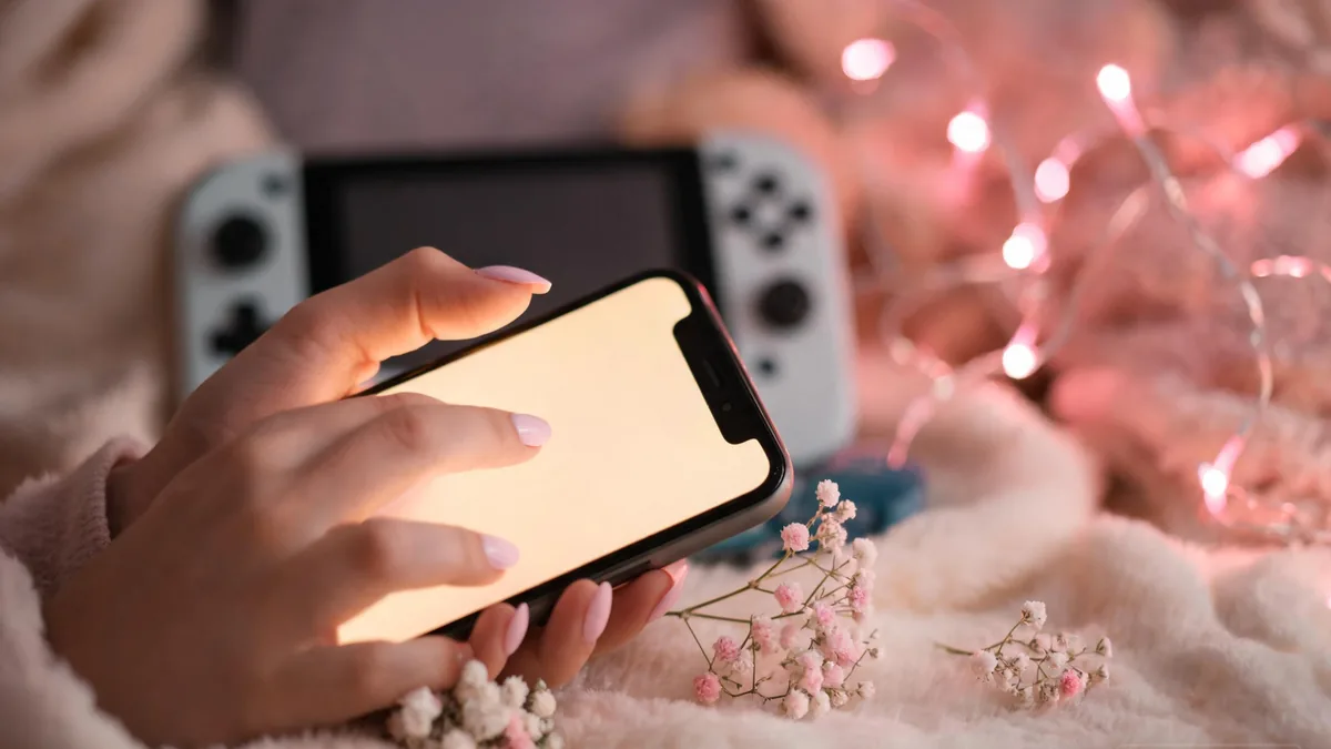 Otome-style AI companion play on a phone, with soft warm light, a handheld console nearby, and a cozy evening atmosphere
