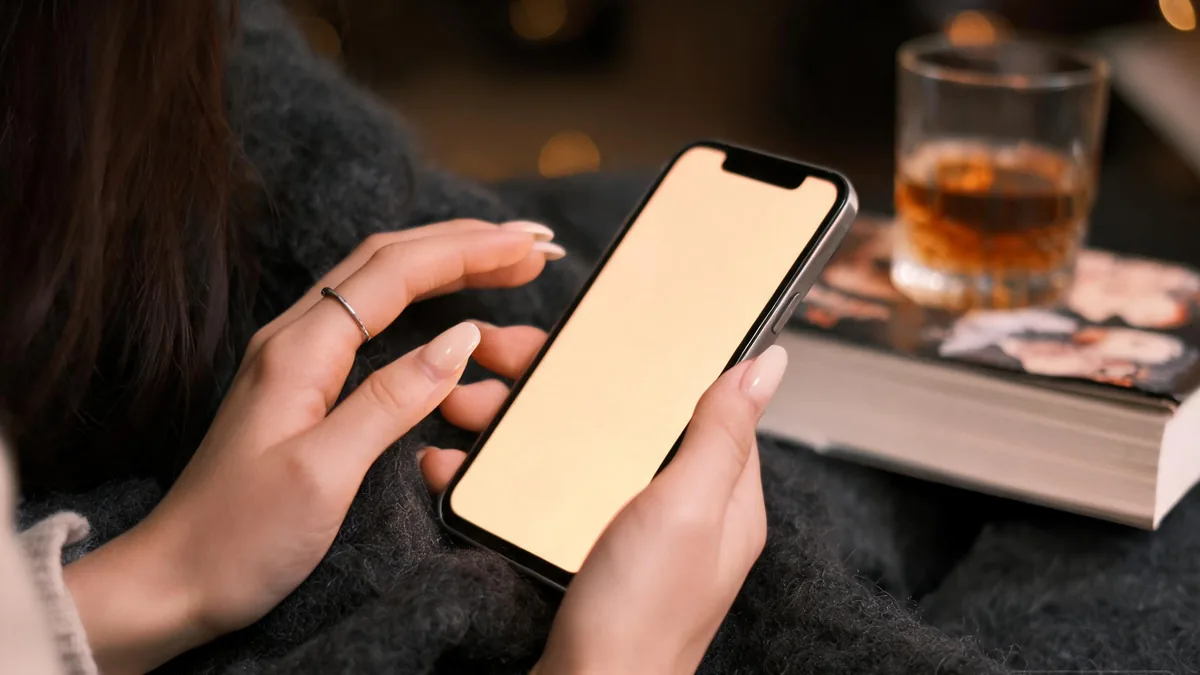 A hand resting beside a softly glowing phone, an open graphic novel, and a coffee mug on a dark wood desk, a quiet seinen-flavored evening with an AI companion