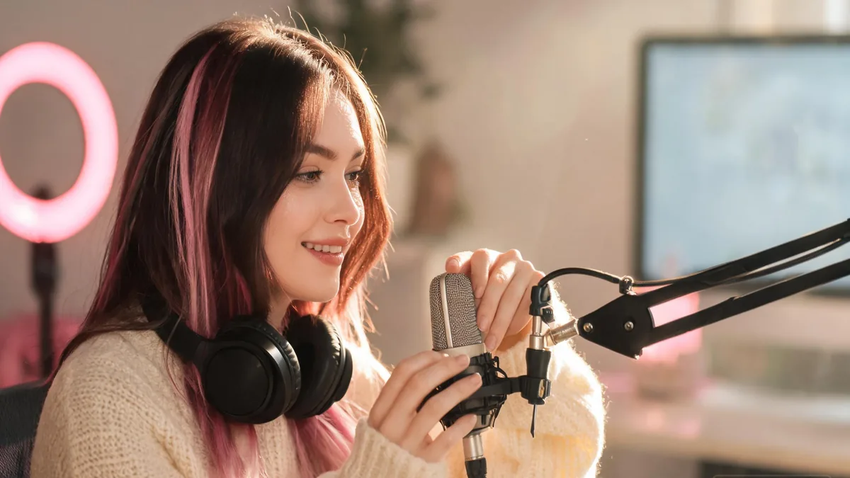 VTuber-style streamer with pastel hair and headphones smiling at her microphone, the warm, friendly streamer energy that defines the format